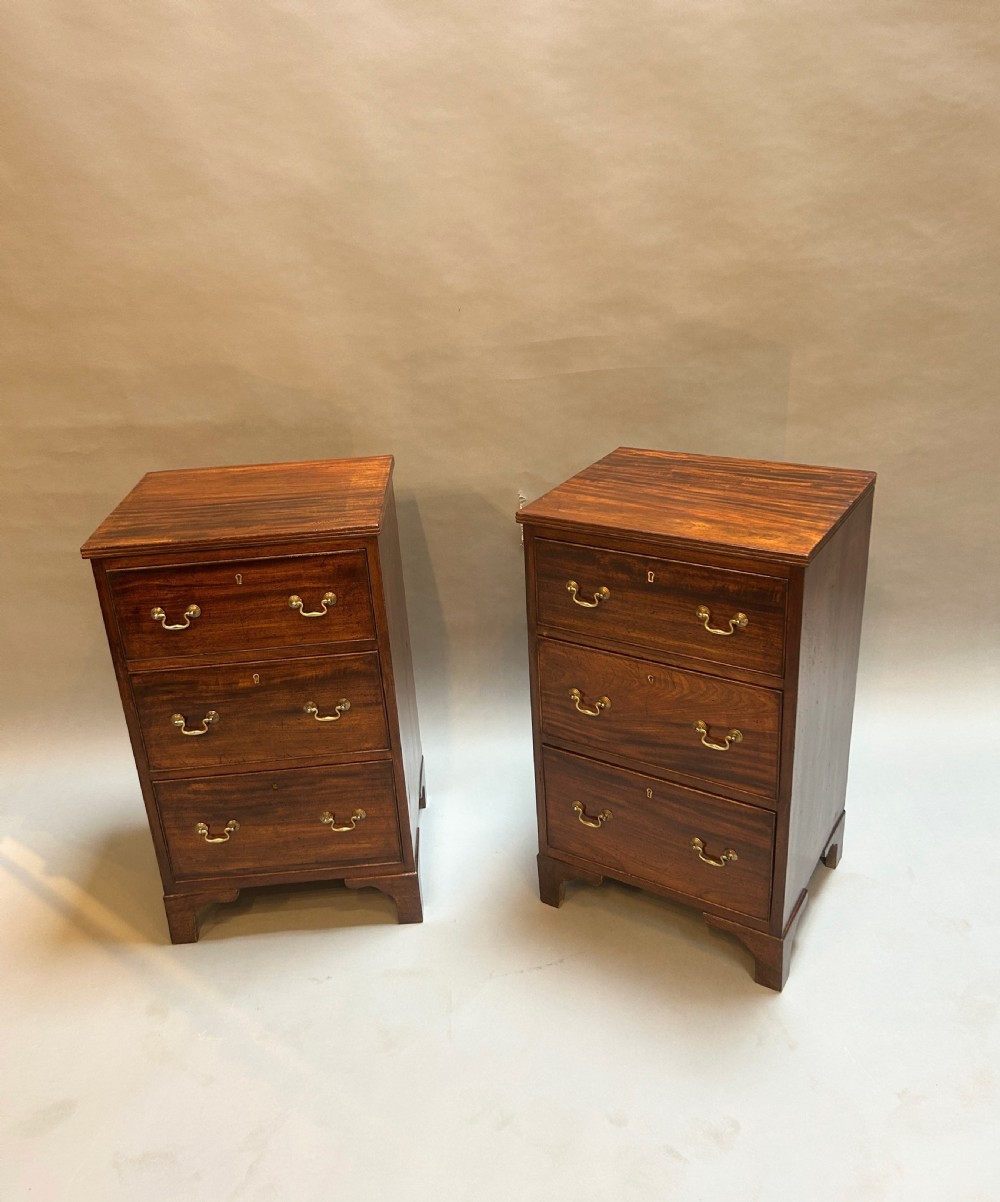 A matching pair of three-drawer dark mahogany bedside chests featuring brass swan-neck handles and bracket feet.