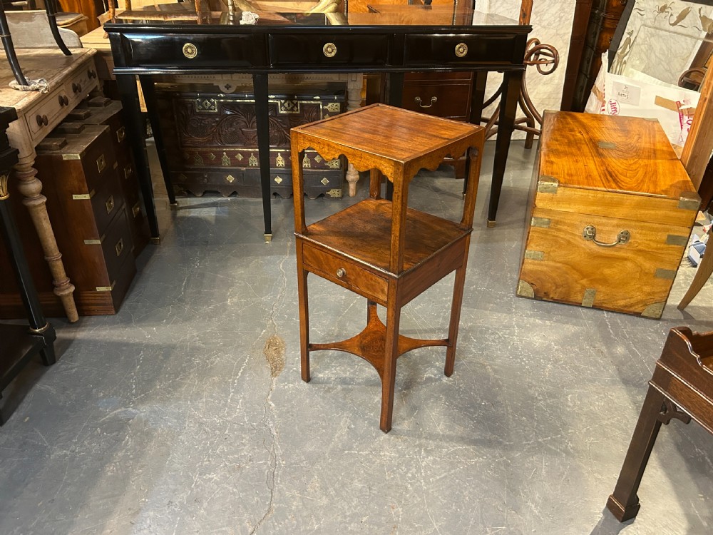 A George III mahogany nightstand featuring a shaped gallery top tier, an open middle shelf, a single drawer with a brass knob, and a shaped cross stretcher at the base. View X