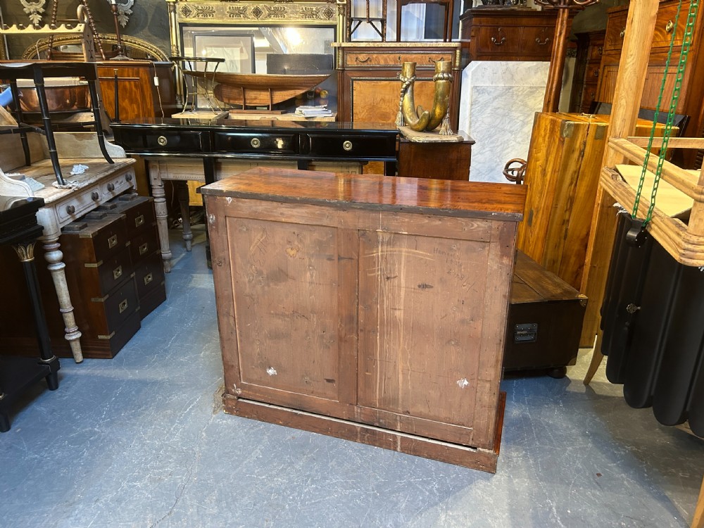 A Regency mahogany side cabinet featuring flame veneer, two panelled doors, brass stringing inlay, and gilt metal Egyptian bust mounts. View X