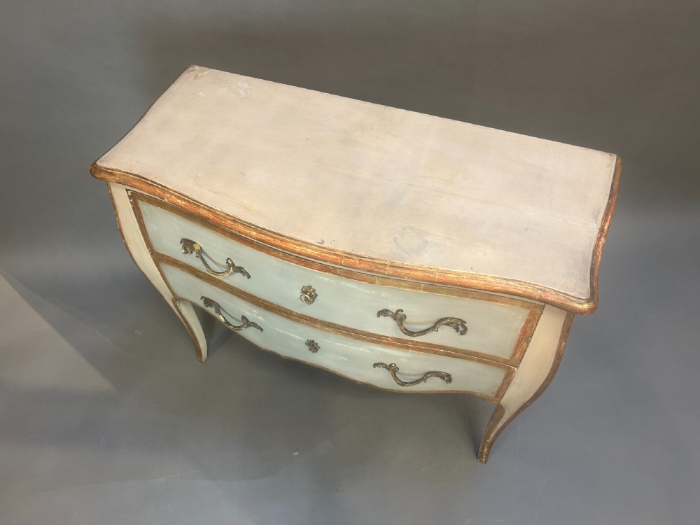 A French Louis XV style painted and gilt serpentine commode featuring two drawers, gold leaf borders, and curved cabriole legs. View II