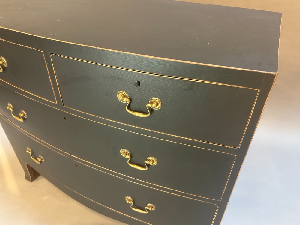 A Regency period ebonised bow-front chest of drawers featuring two short over two long drawers with brass drop handles and bracket feet. View II