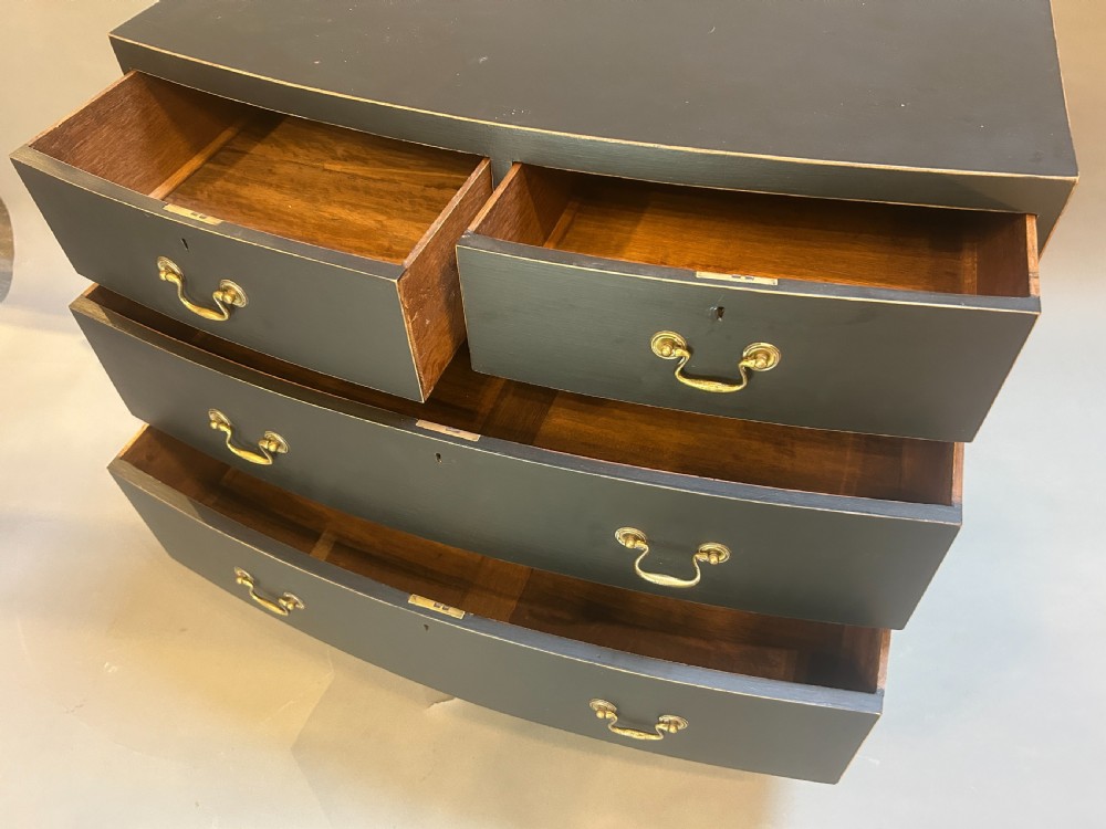 A Regency period ebonised bow-front chest of drawers featuring two short over two long drawers with brass drop handles and bracket feet. View V