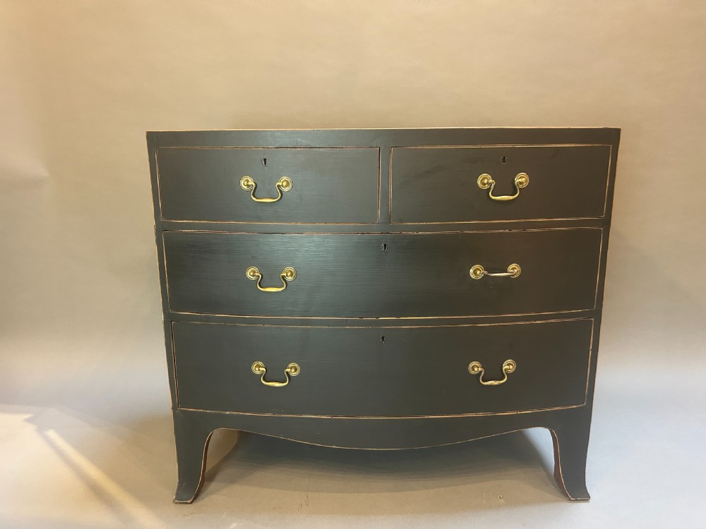 A Regency period ebonised bow-front chest of drawers featuring two short over two long drawers with brass drop handles and bracket feet. View VII