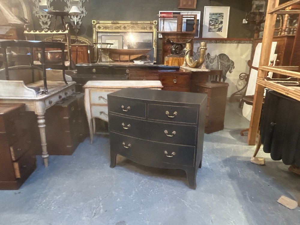 A Regency period ebonised bow-front chest of drawers featuring two short over two long drawers with brass drop handles and bracket feet. View VIII