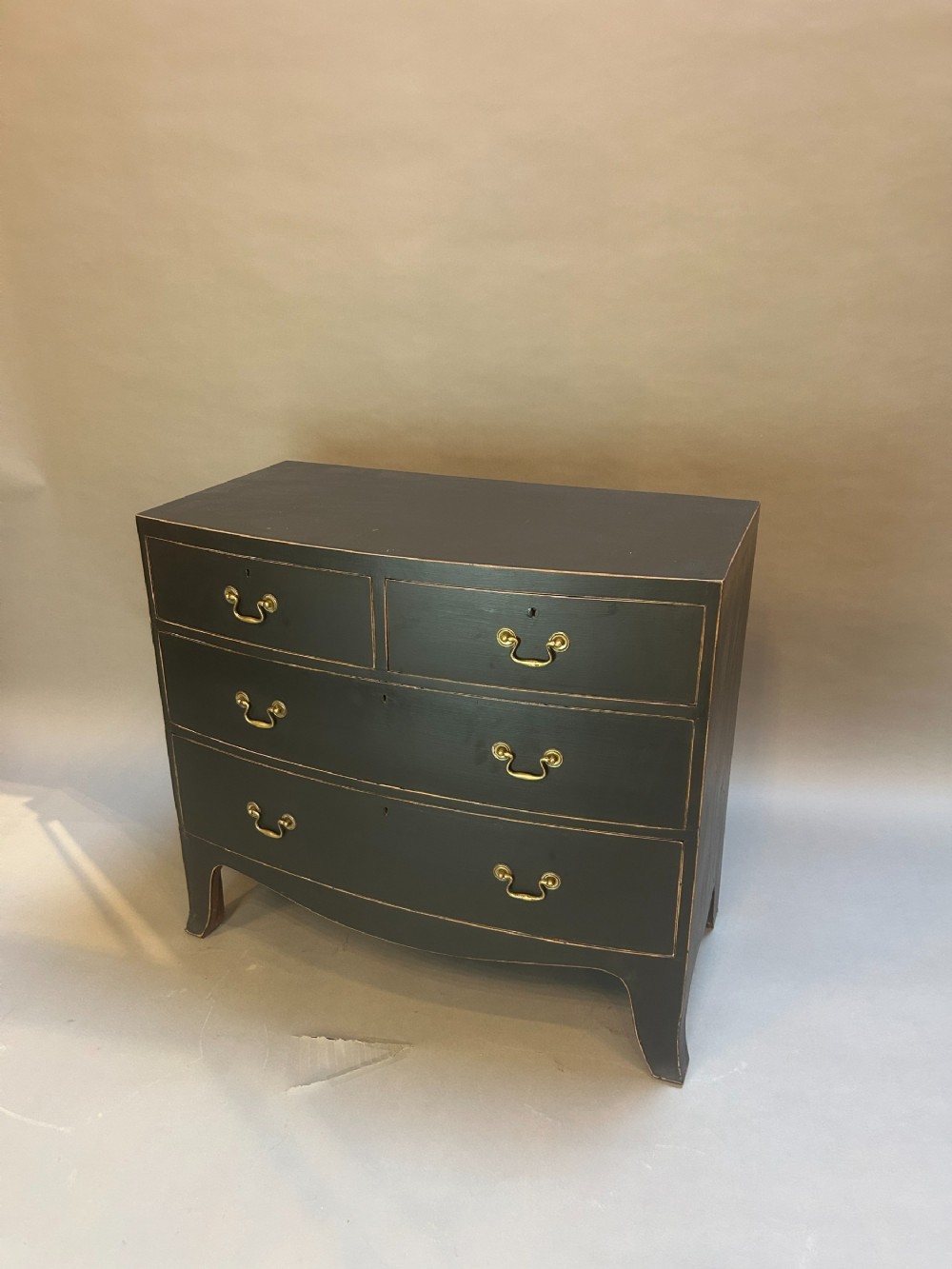 A Regency period ebonised bow-front chest of drawers featuring two short over two long drawers with brass drop handles and bracket feet.
