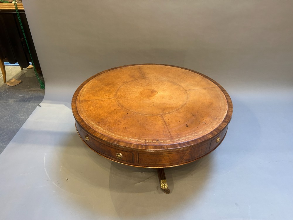 A low circular mahogany drum table featuring a gold-tooled leather top, frieze drawers with brass pulls, and a pedestal base with brass lion paw castors. View II