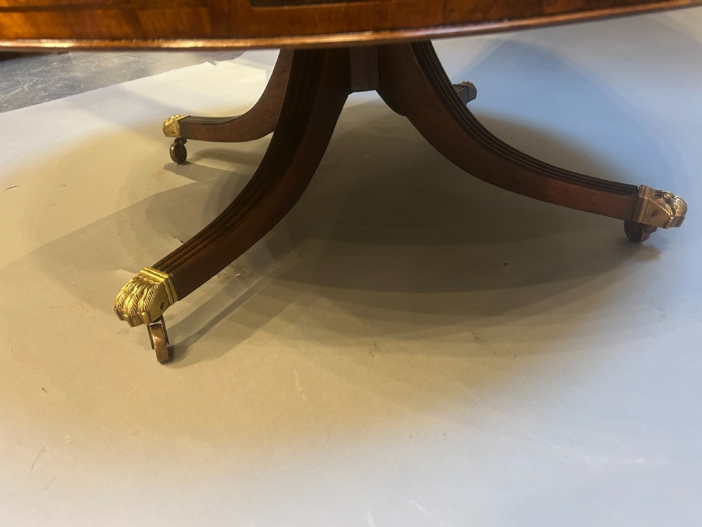 A low circular mahogany drum table featuring a gold-tooled leather top, frieze drawers with brass pulls, and a pedestal base with brass lion paw castors. View V