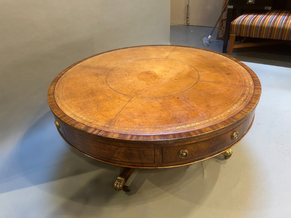 A low circular mahogany drum table featuring a gold-tooled leather top, frieze drawers with brass pulls, and a pedestal base with brass lion paw castors. View VI