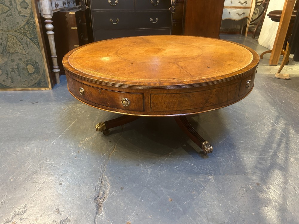 A low circular mahogany drum table featuring a gold-tooled leather top, frieze drawers with brass pulls, and a pedestal base with brass lion paw castors. View VII