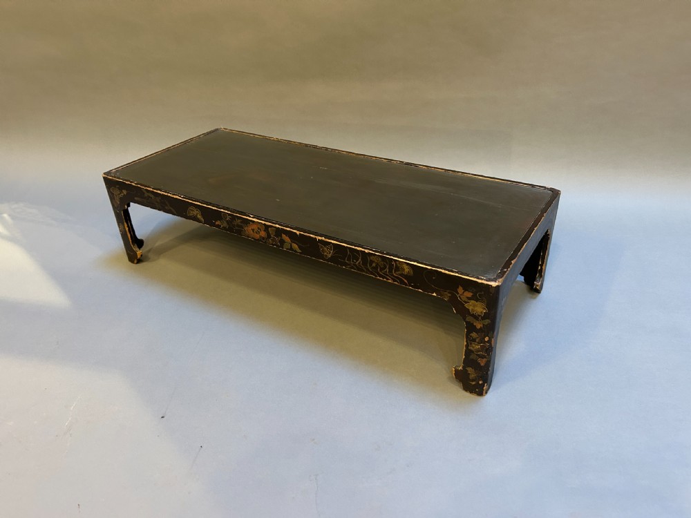 A low rectangular antique Chinese black lacquered coffee table decorated with hand-painted floral motifs and corner apron detail.