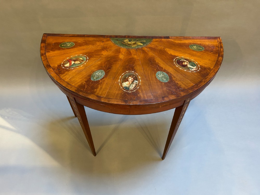 A 19th-century Sheraton style demilune card table featuring painted portrait ovals, fan marquetry, and tapered legs. View IV