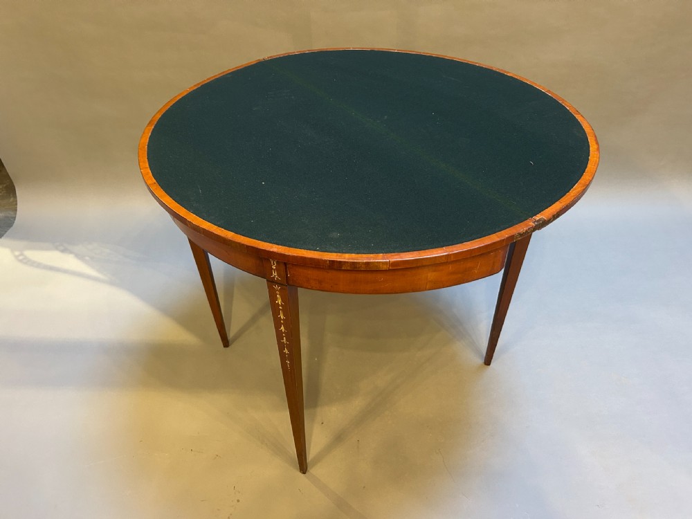 A 19th-century Sheraton style demilune card table featuring painted portrait ovals, fan marquetry, and tapered legs. View V