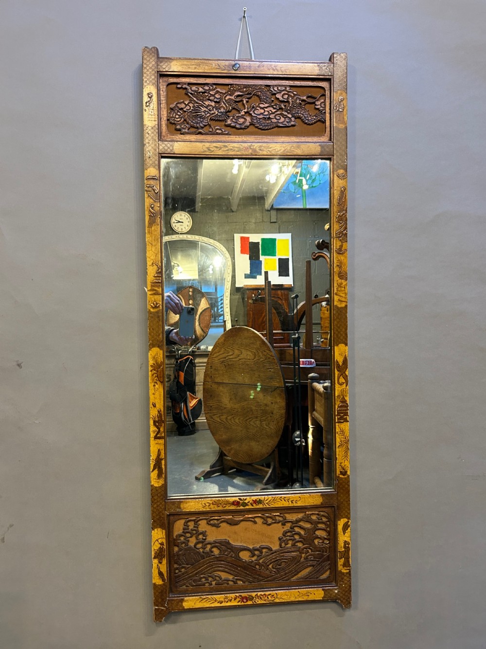 A tall, narrow timber wall mirror decorated with relief carvings of dragons and waves at the top and bottom, framed by gilt painted chinoiserie side borders.
