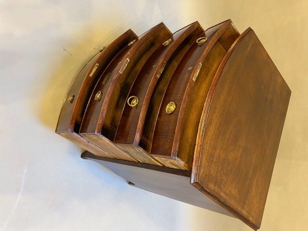 An Edwardian mahogany bow-front chest of drawers with four graduated drawers, circular brass handles, and splayed bracket feet. View IV