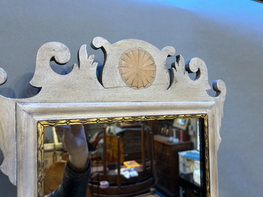 A fret-cut wall mirror featuring a pale bleached wood frame with a scrolled cresting silhouette, central carved patera motif, and a gilded inner rim holding rectangular glass. View II