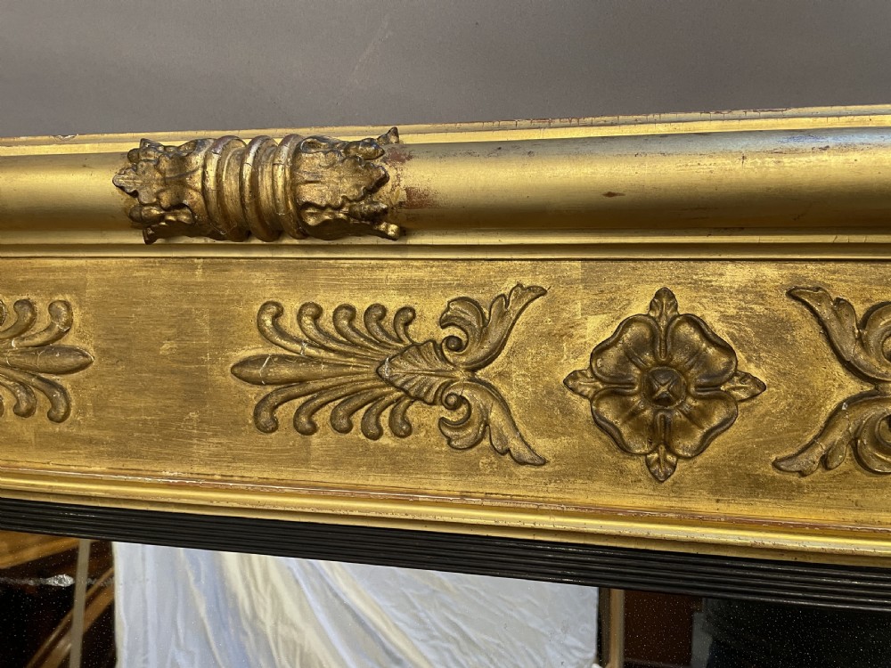 A large horizontal Regency gilt overmantel mirror featuring neoclassical side columns, a frieze with carved palmettes and rosettes, and an ebonised inner slip. View IV