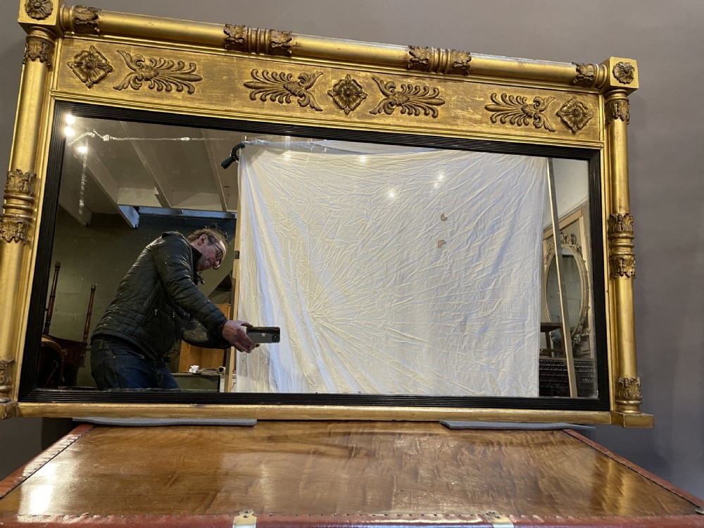 A large horizontal Regency gilt overmantel mirror featuring neoclassical side columns, a frieze with carved palmettes and rosettes, and an ebonised inner slip. View XII