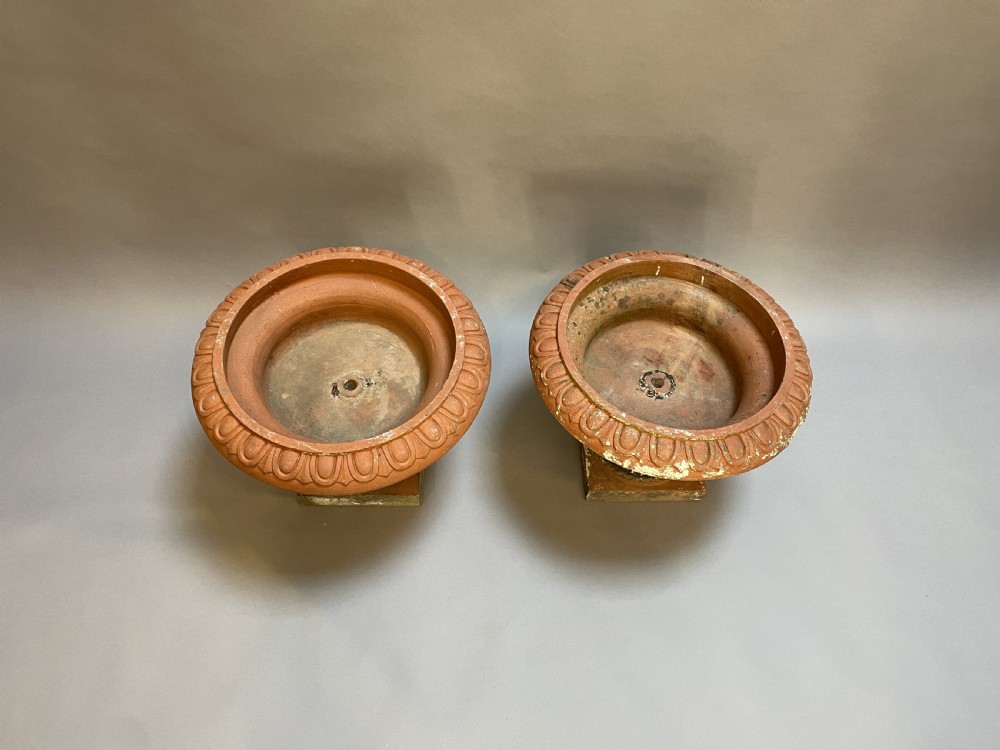 A pair of weathered terracotta Campana garden urns featuring wide egg-and-dart rims, gadrooned lower bowls, fluted stems, and square bases. View III