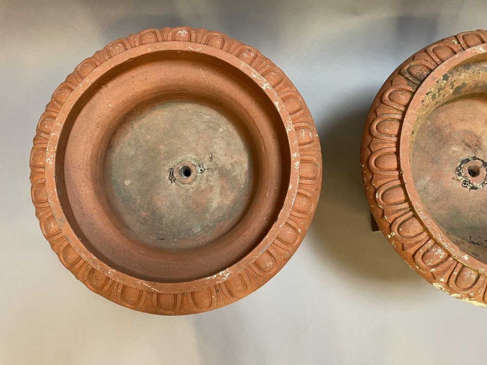 A pair of weathered terracotta Campana garden urns featuring wide egg-and-dart rims, gadrooned lower bowls, fluted stems, and square bases. View V
