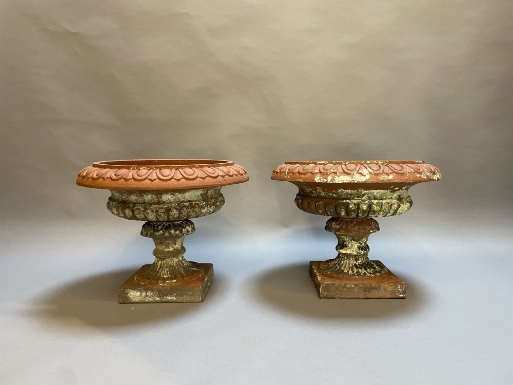 A pair of weathered terracotta Campana garden urns featuring wide egg-and-dart rims, gadrooned lower bowls, fluted stems, and square bases. View VI