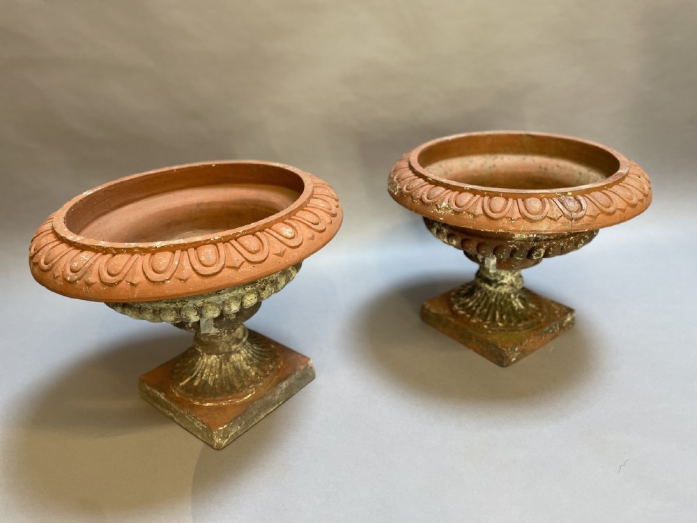 A pair of weathered terracotta Campana garden urns featuring wide egg-and-dart rims, gadrooned lower bowls, fluted stems, and square bases. View VII