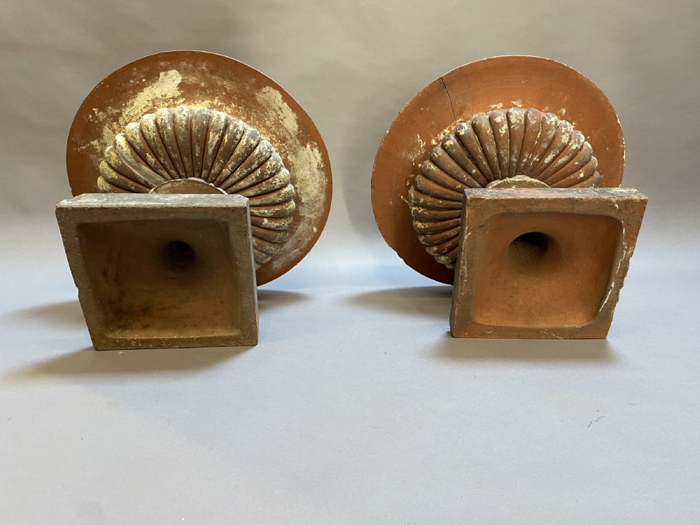 A pair of weathered terracotta Campana garden urns featuring wide egg-and-dart rims, gadrooned lower bowls, fluted stems, and square bases. View X