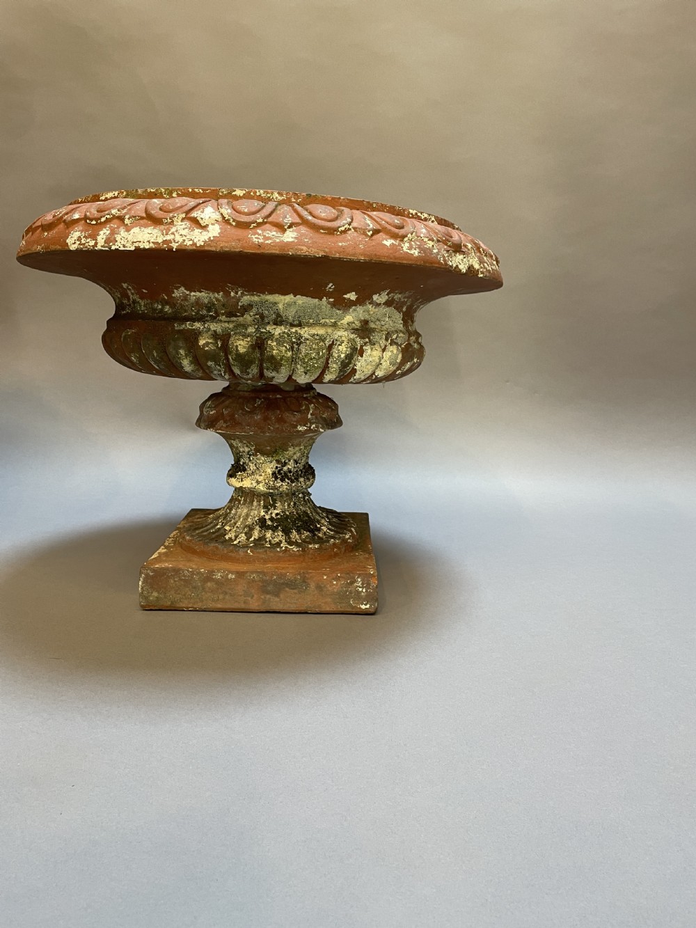 A pair of weathered terracotta Campana garden urns featuring wide egg-and-dart rims, gadrooned lower bowls, fluted stems, and square bases. View XII