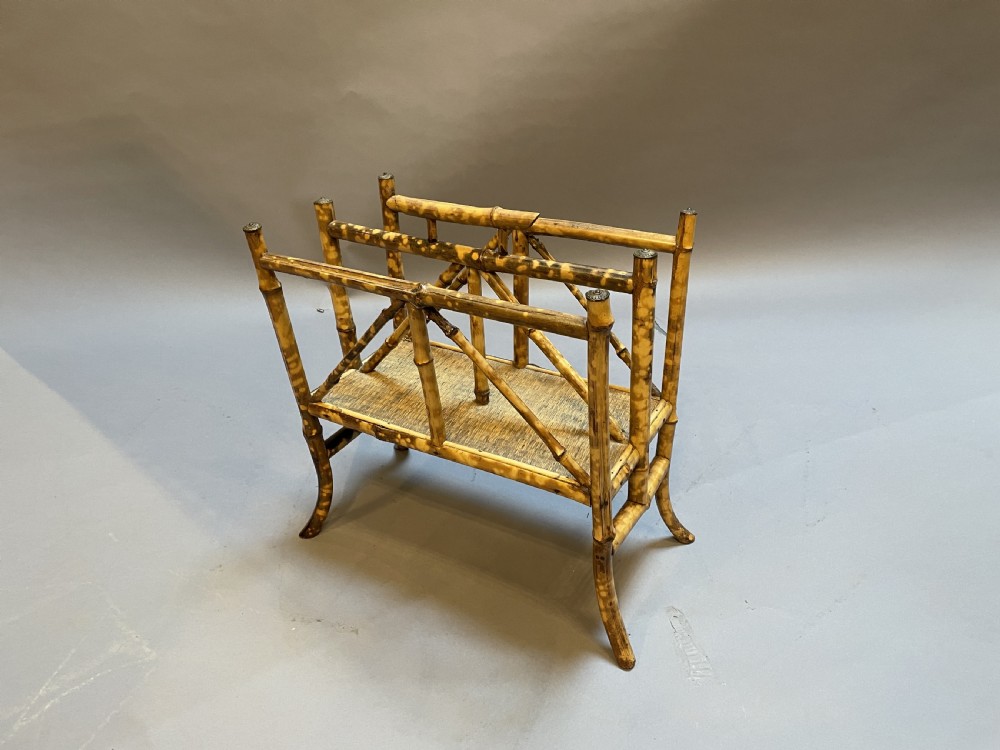 A late 19th-century bamboo canterbury rack featuring diagonal cross-bracing, a woven lower shelf, four partitioned sections, and metal capped finials.