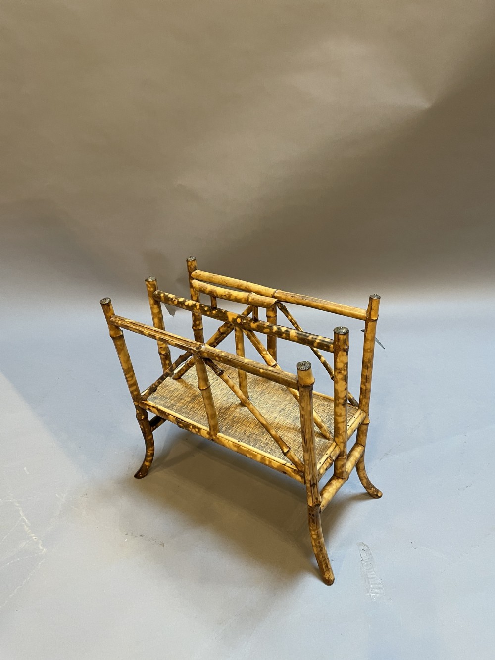 A late 19th-century bamboo canterbury rack featuring diagonal cross-bracing, a woven lower shelf, four partitioned sections, and metal capped finials. View II