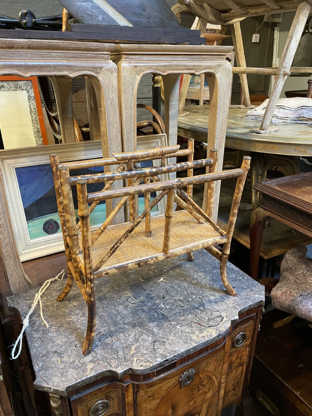 A late 19th-century bamboo canterbury rack featuring diagonal cross-bracing, a woven lower shelf, four partitioned sections, and metal capped finials. View VI