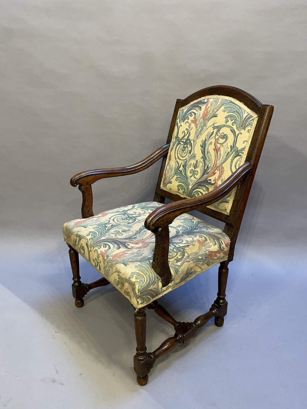 A 19th-century French fauteuil armchair with a carved dark wooden frame, open curved arms, turned stretchers, and leafy tapestry upholstery.