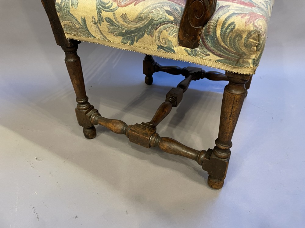 A 19th-century French fauteuil armchair with a carved dark wooden frame, open curved arms, turned stretchers, and leafy tapestry upholstery. View V