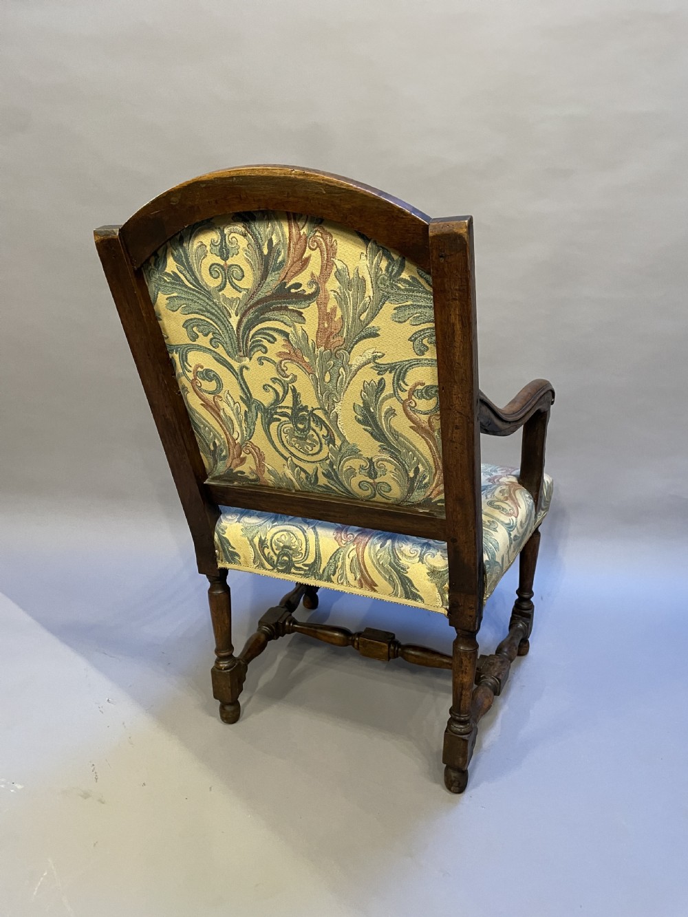 A 19th-century French fauteuil armchair with a carved dark wooden frame, open curved arms, turned stretchers, and leafy tapestry upholstery. View VI