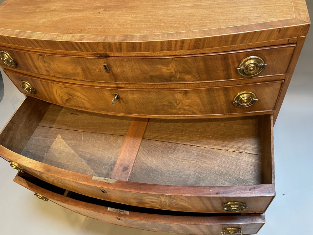 An antique Regency bow-front mahogany chest featuring four graduated drawers with circular brass ring handles on splayed bracket feet. View II