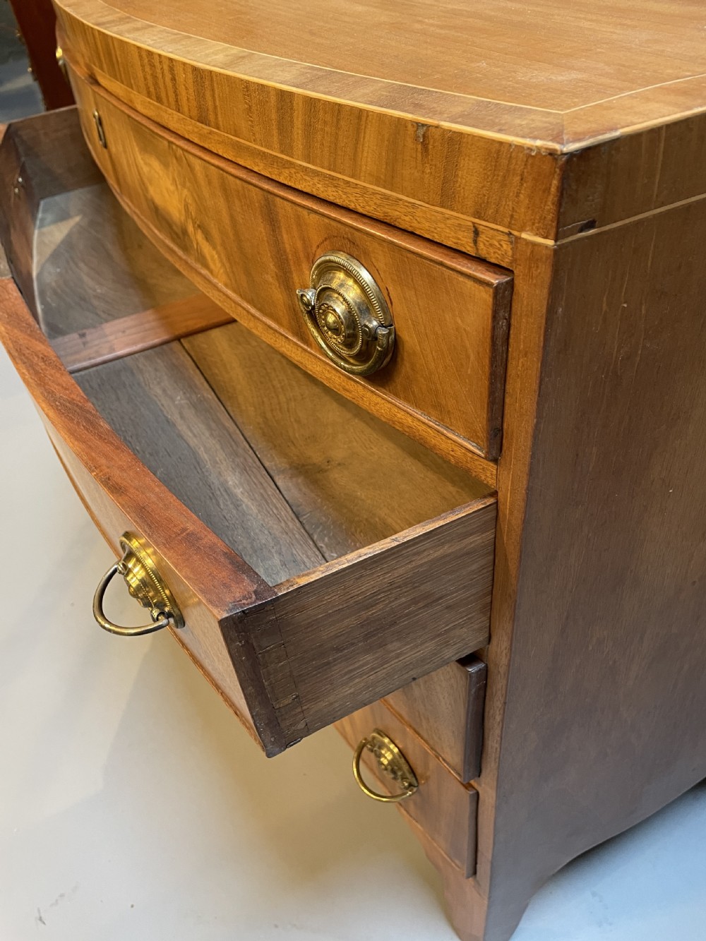 An antique Regency bow-front mahogany chest featuring four graduated drawers with circular brass ring handles on splayed bracket feet. View III