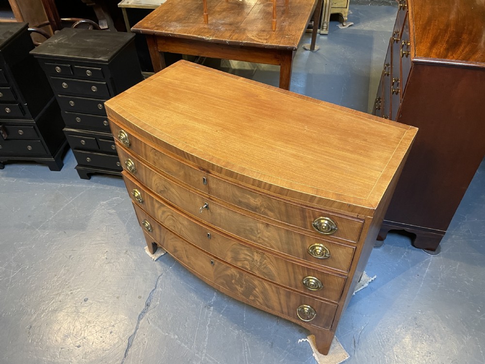 An antique Regency bow-front mahogany chest featuring four graduated drawers with circular brass ring handles on splayed bracket feet. View V