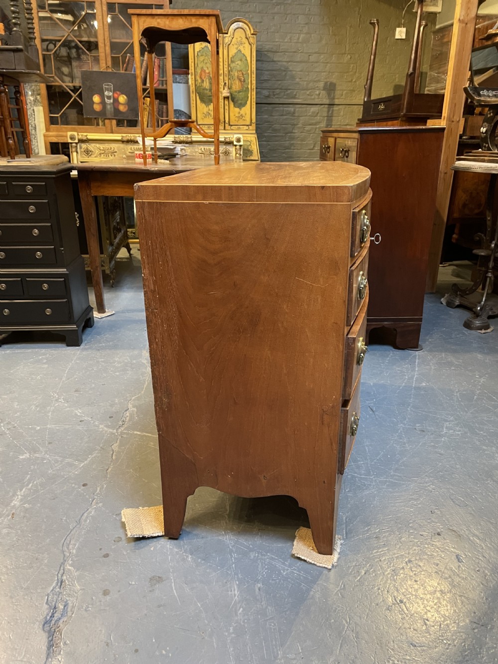 An antique Regency bow-front mahogany chest featuring four graduated drawers with circular brass ring handles on splayed bracket feet. View VII