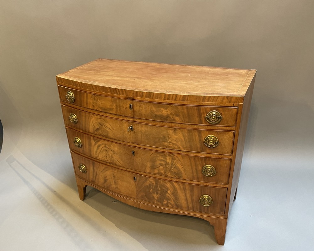 An antique Regency bow-front mahogany chest featuring four graduated drawers with circular brass ring handles on splayed bracket feet. View VIII