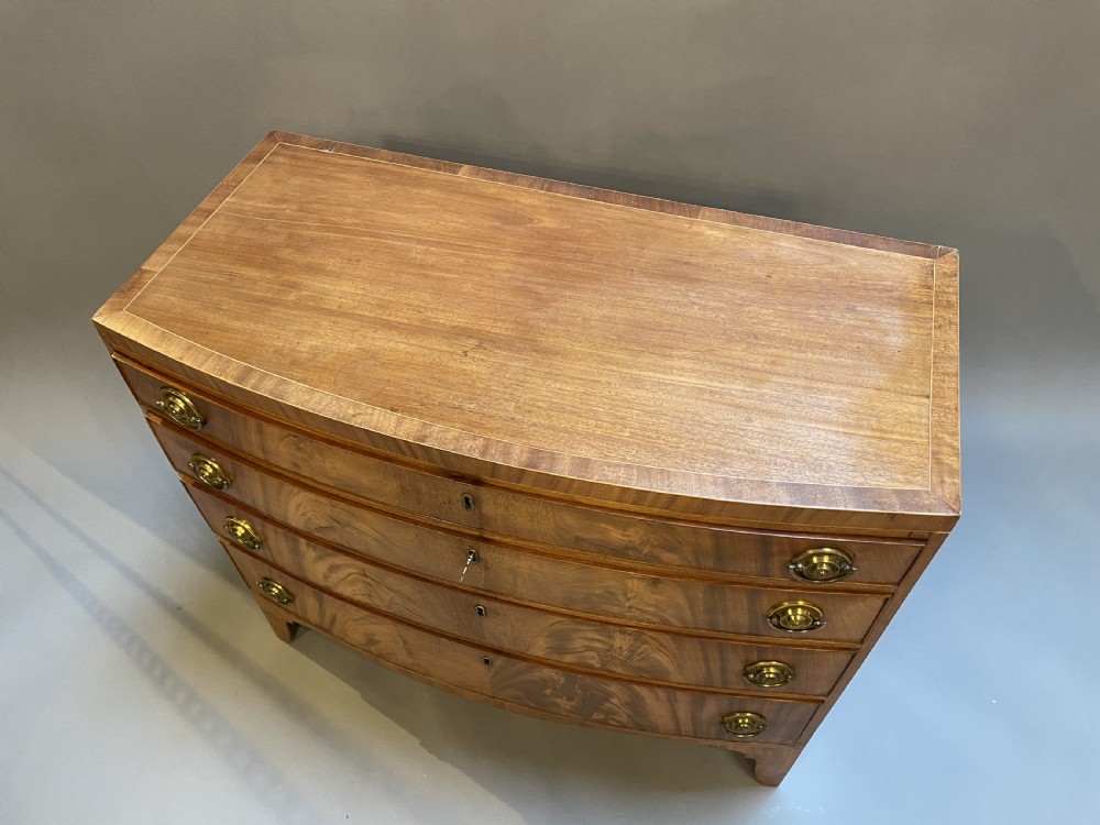 An antique Regency bow-front mahogany chest featuring four graduated drawers with circular brass ring handles on splayed bracket feet. View IX