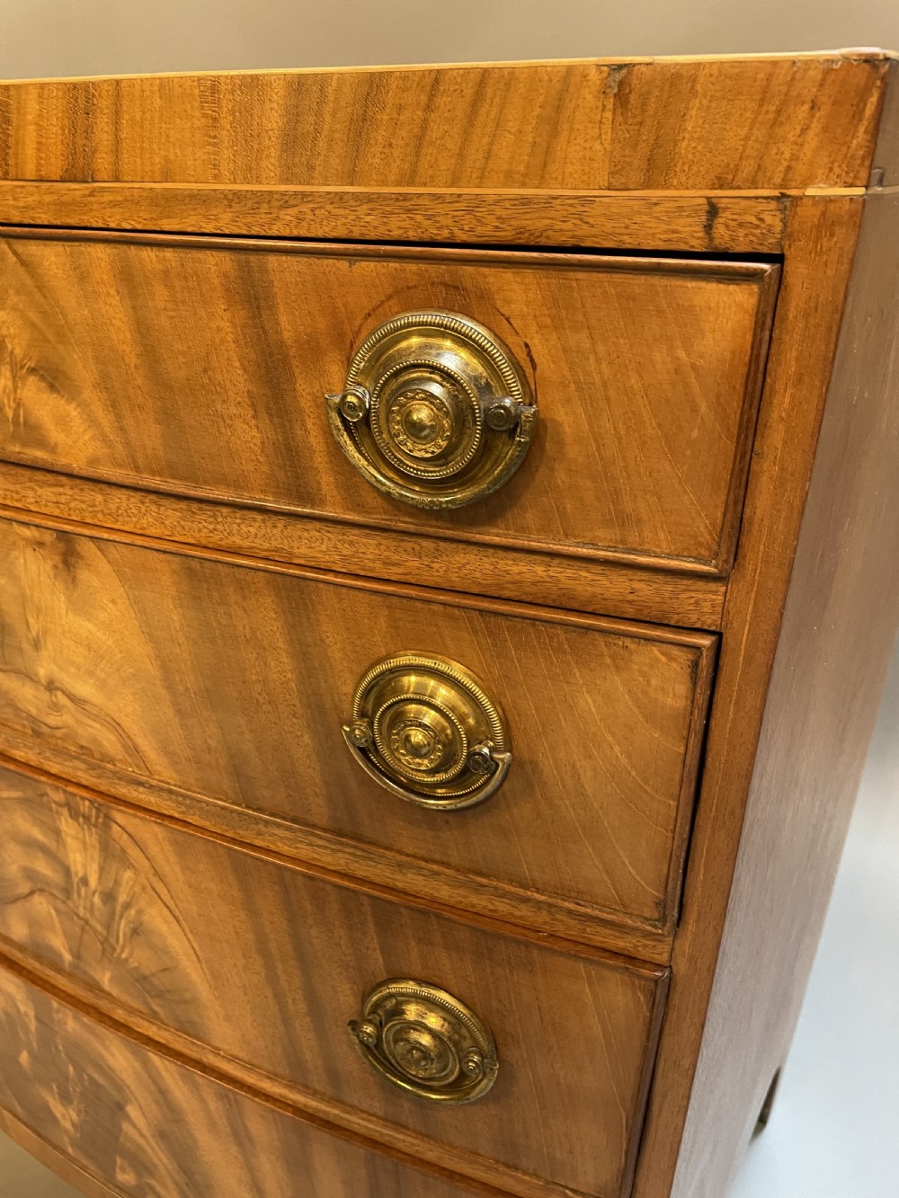 An antique Regency bow-front mahogany chest featuring four graduated drawers with circular brass ring handles on splayed bracket feet. View X