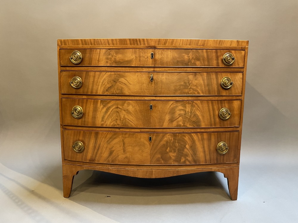 An antique Regency bow-front mahogany chest featuring four graduated drawers with circular brass ring handles on splayed bracket feet. View XI