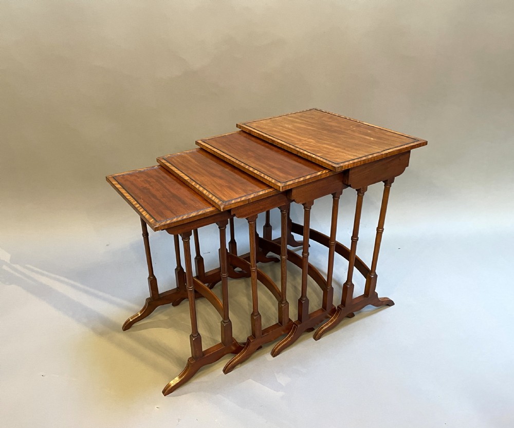 A set of four Edwardian mahogany nesting tables with turned legs, arched stretchers, and inlaid wood borders, arranged in a stepped cascade. View II