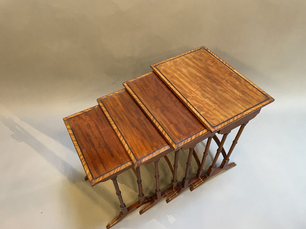 A set of four Edwardian mahogany nesting tables with turned legs, arched stretchers, and inlaid wood borders, arranged in a stepped cascade. View III