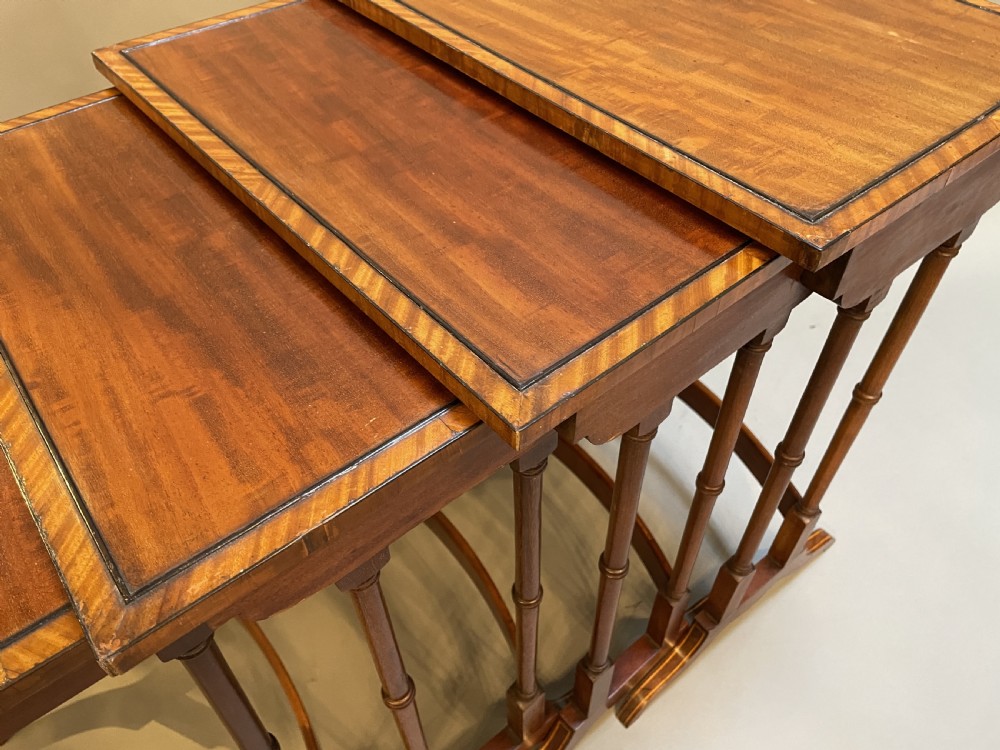 A set of four Edwardian mahogany nesting tables with turned legs, arched stretchers, and inlaid wood borders, arranged in a stepped cascade. View IV