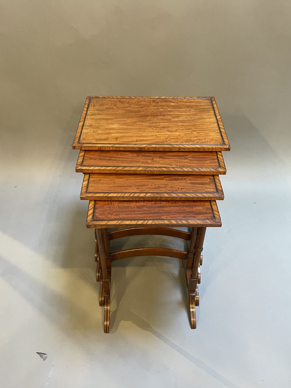 A set of four Edwardian mahogany nesting tables with turned legs, arched stretchers, and inlaid wood borders, arranged in a stepped cascade. View VIII
