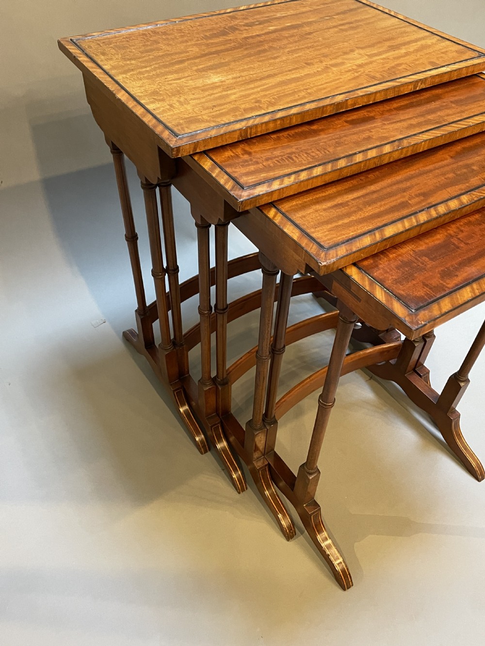 A set of four Edwardian mahogany nesting tables with turned legs, arched stretchers, and inlaid wood borders, arranged in a stepped cascade. View IX