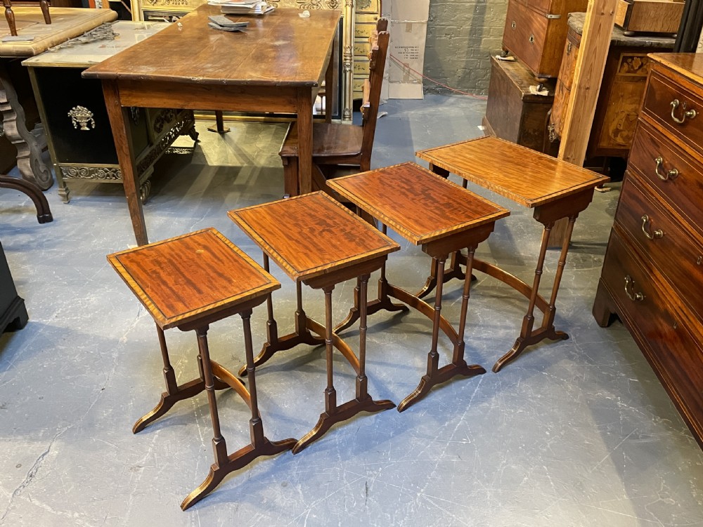 A set of four Edwardian mahogany nesting tables with turned legs, arched stretchers, and inlaid wood borders, arranged in a stepped cascade. View X