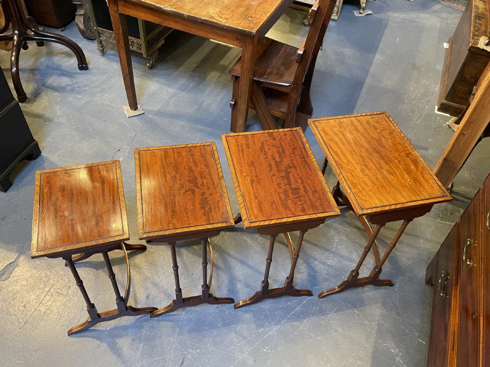 A set of four Edwardian mahogany nesting tables with turned legs, arched stretchers, and inlaid wood borders, arranged in a stepped cascade. View XII