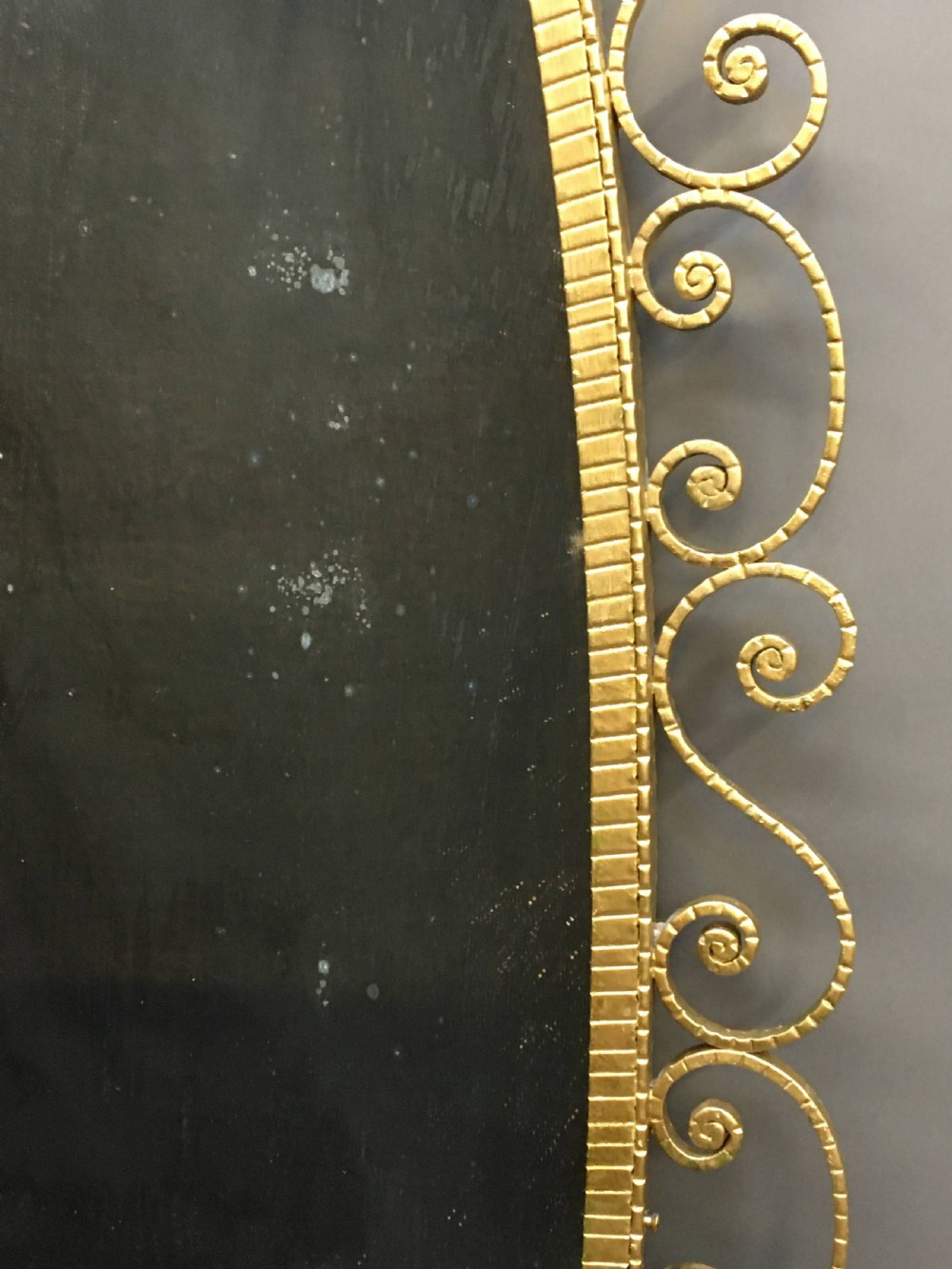 A tall oval wall mirror featuring a gilded metal frame with scrollwork bordering the edge and cresting at the top and bottom. View VII
