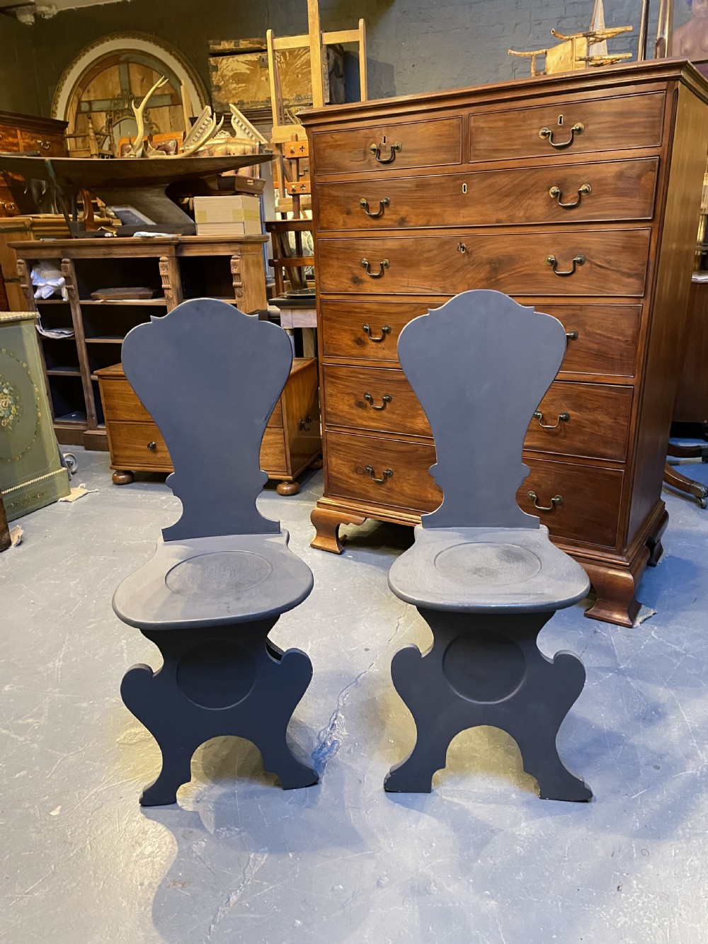 A pair of grey painted wooden Sgabello hall chairs featuring shaped cartouche backs and carved trestle supports. View V